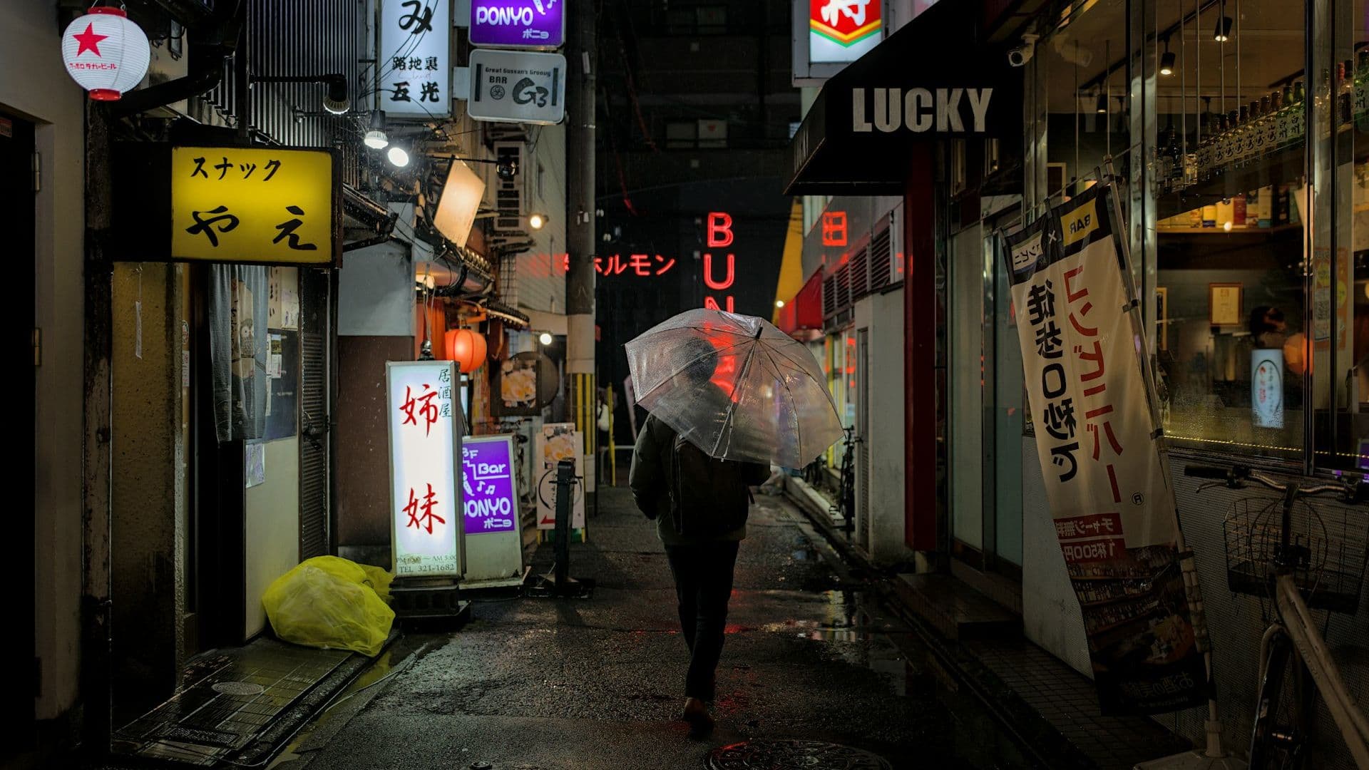 Person with umbrella walking down a rain-lit alley at night